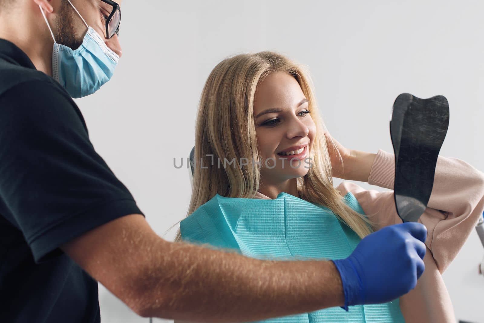 Portrait of a dentist in eyeglasses who treats teeth of young blond woman patient.