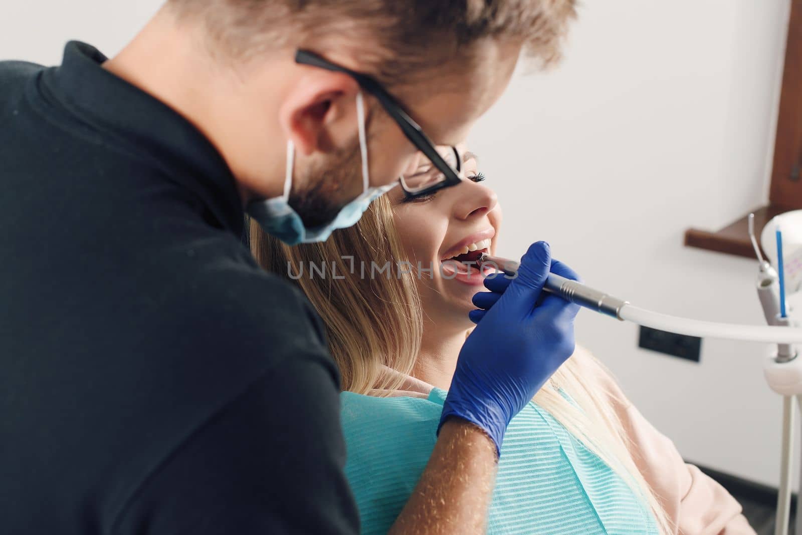 Portrait of a dentist in eyeglasses who treats teeth of young blond woman patient.