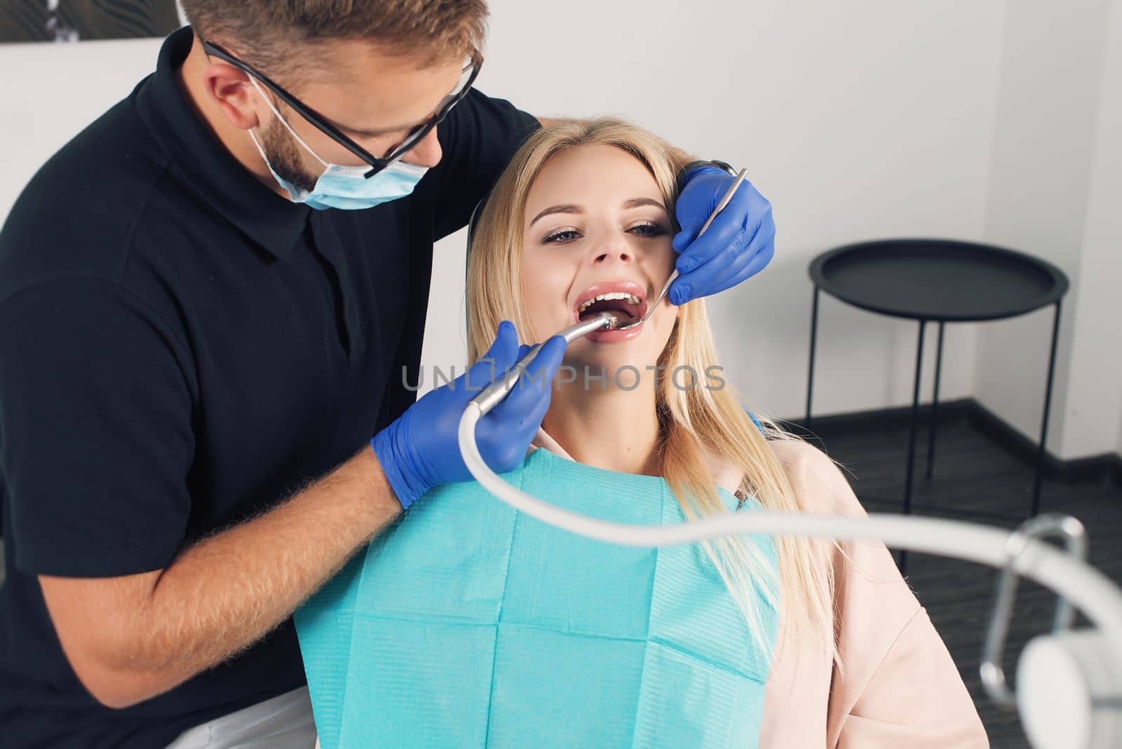 Portrait of a dentist in eyeglasses who treats teeth of young blond woman patient.