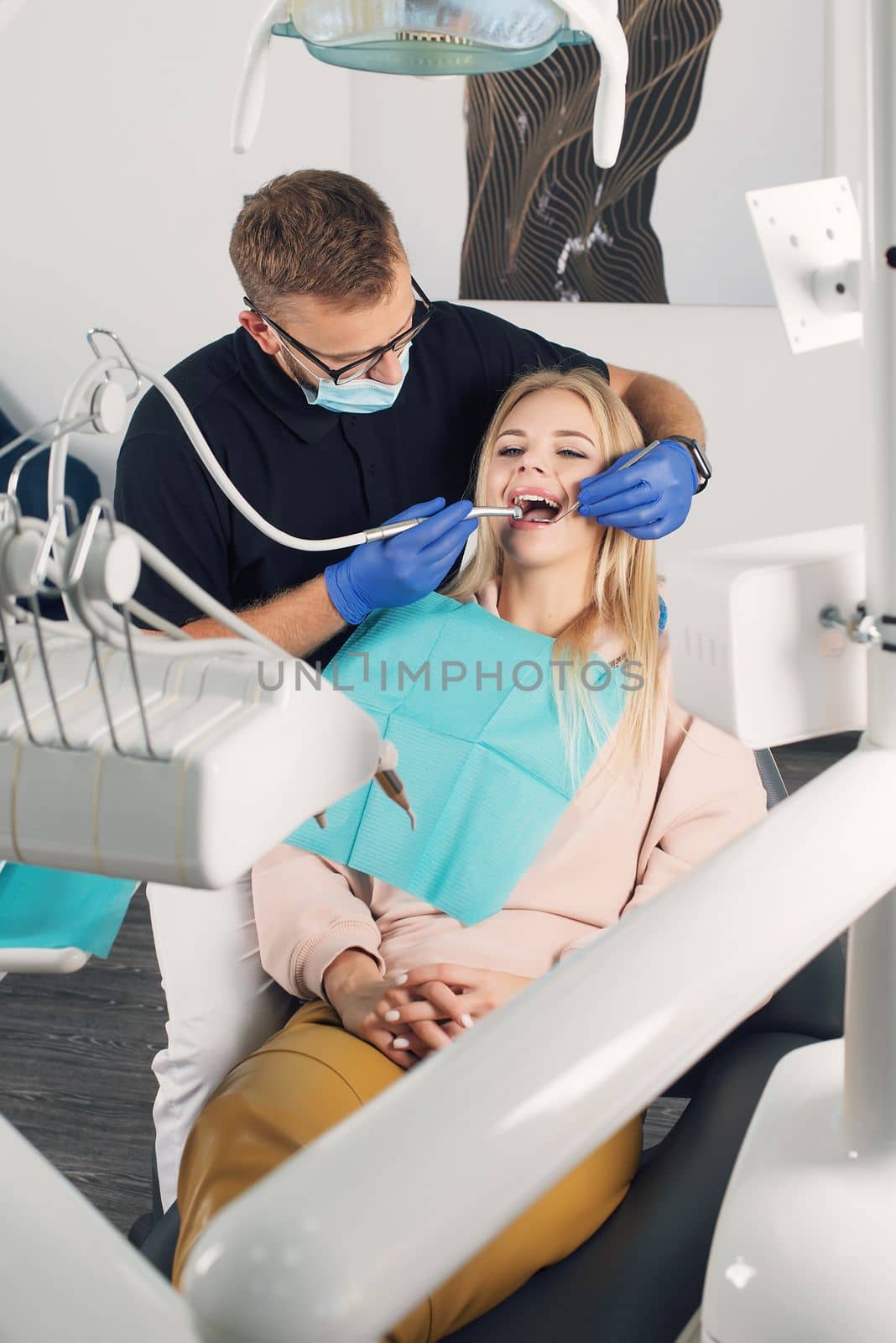 Portrait of a dentist in eyeglasses who treats teeth of young blond woman patient.