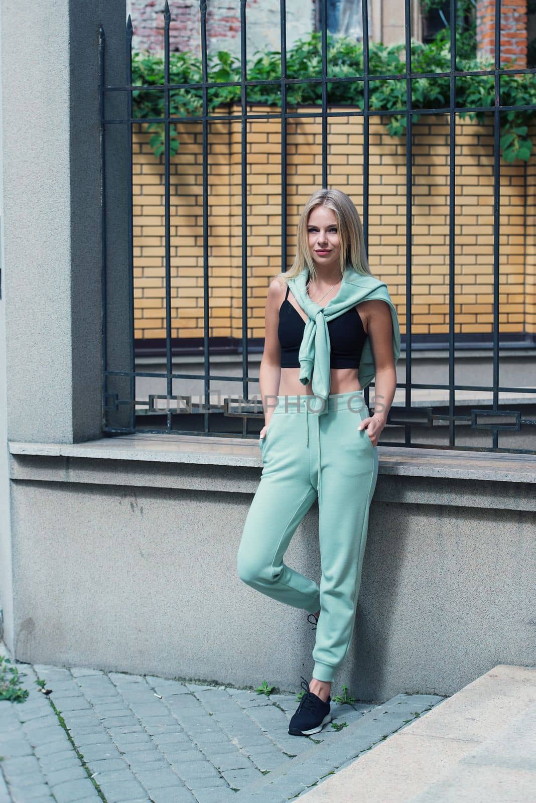 Stylish beautiful young blond woman in a light green tracksuit posing on the street. Attractive girl model posing outdoors by Ashtray25