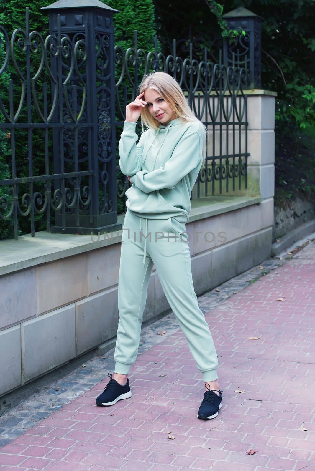 Stylish beautiful young blond woman in a light green tracksuit posing on the street. Attractive girl model posing outdoors. Fitness lady