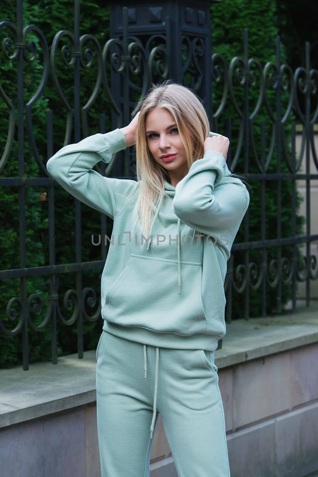 Stylish beautiful young blond woman in a light green tracksuit posing on the street. Attractive girl model posing outdoors. Fitness lady