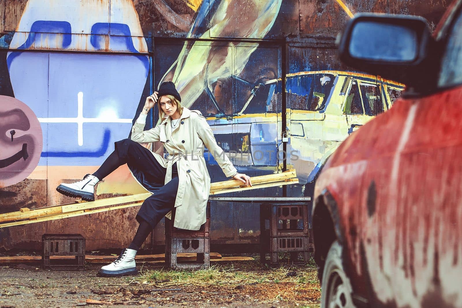 stylish blonde woman wearing long beige coat, white boots, black hat and backpack posing through the city streets. Selective focus, grain by Ashtray25