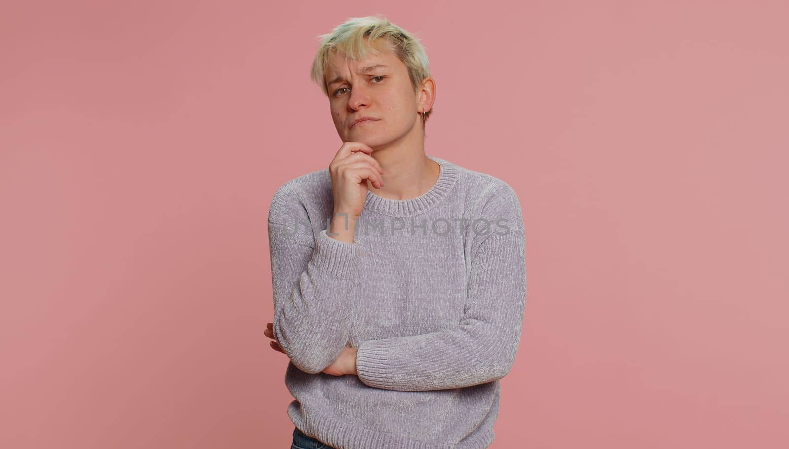 Thoughtful clever millennial woman with short hair rubbing chin and looking aside with pensive expression, pondering a solution, doubting question. Young girl on pink background. Lgbt lesbian people