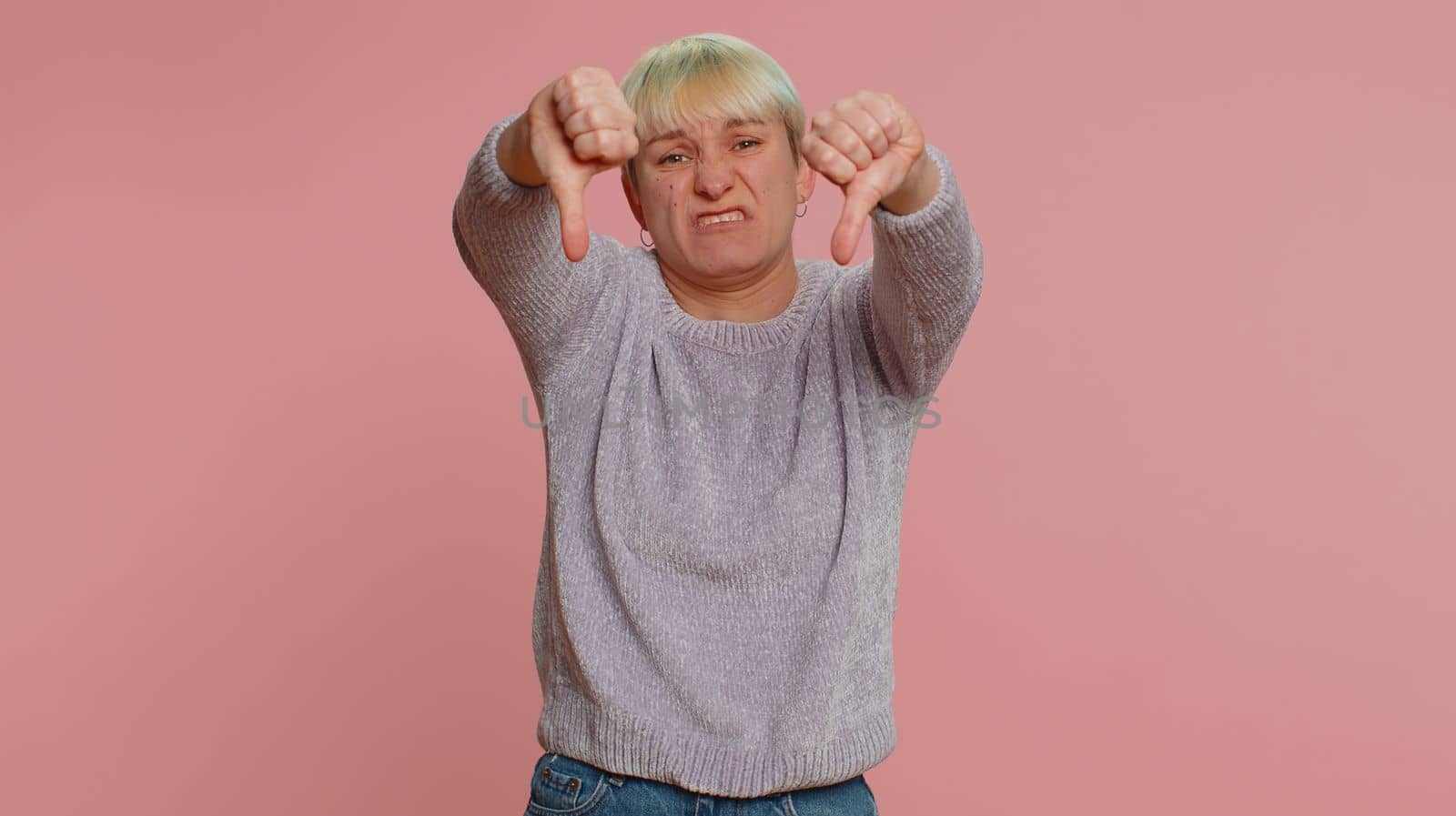 Dislike. Upset unhappy lovely woman with short hair showing thumbs down sign gesture, expressing discontent, disapproval, dissatisfied, dislike. Young girl on pink background. Lgbt gay lesbian people