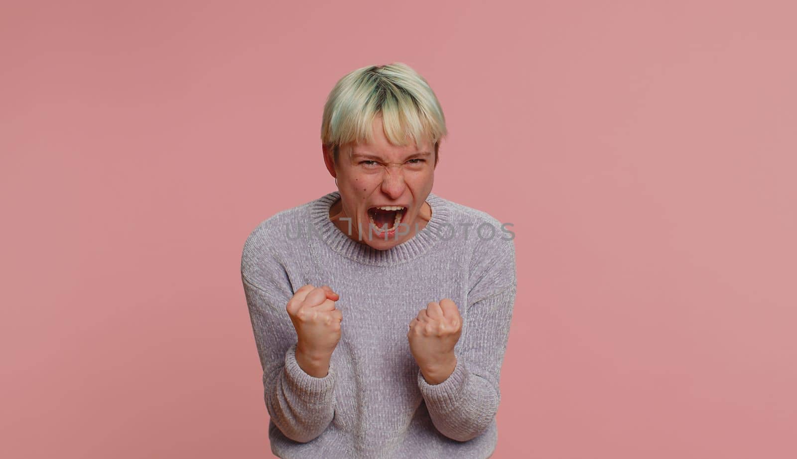 Woman with short green hair screams yell from stress tension problems feels horror hopelessness fear panic surprise shock expresses gestures rage. Girl on pink background. Lgbt gay lesbian people