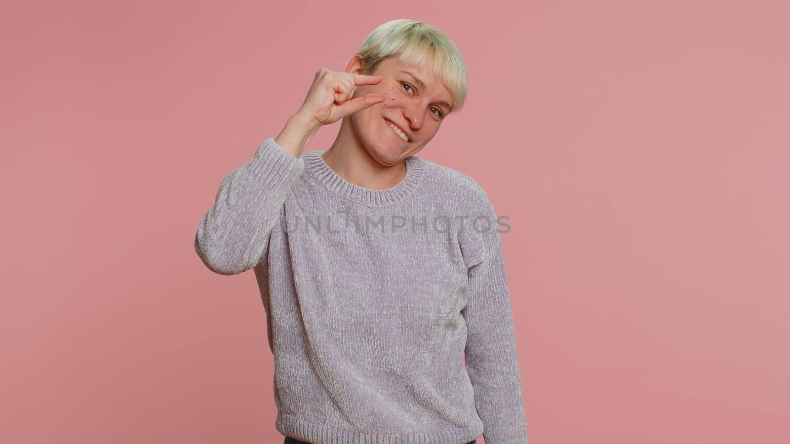 Need some more, please give me. Woman with short hair showing a little bit gesture with sceptic smile, showing minimum sign measuring small size. Young girl on pink background. Lgbt gay lesbian people