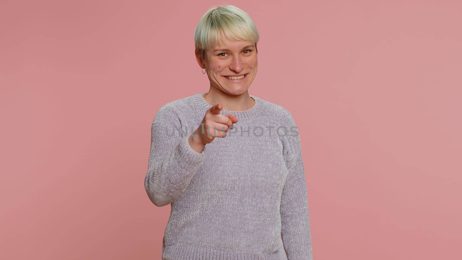 I choose you. Young woman with short hair smiling excitedly, pointing to camera, choosing lucky lottery winner, indicating to awesome you. Girl isolated on pink background. Lgbt gay lesbian people