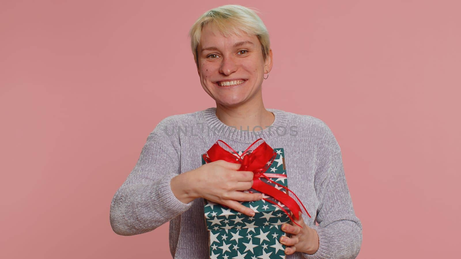 Cheerful woman with short hair opening gift box and smiling joyfully, looking amazed satisfied with nice present, unexpected birthday surprise. Young girl on pink background. Lgbt gay lesbian people