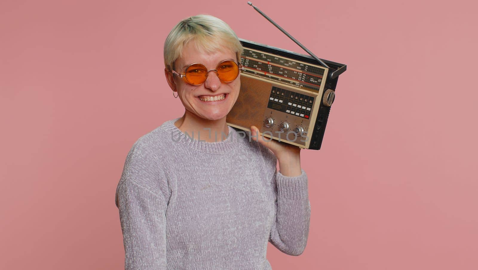 Millennial woman with short hair using retro tape record player to listen music, disco dancing of favorite track, having fun, entertaining, fan of vintage technologies. Young girl on pink background