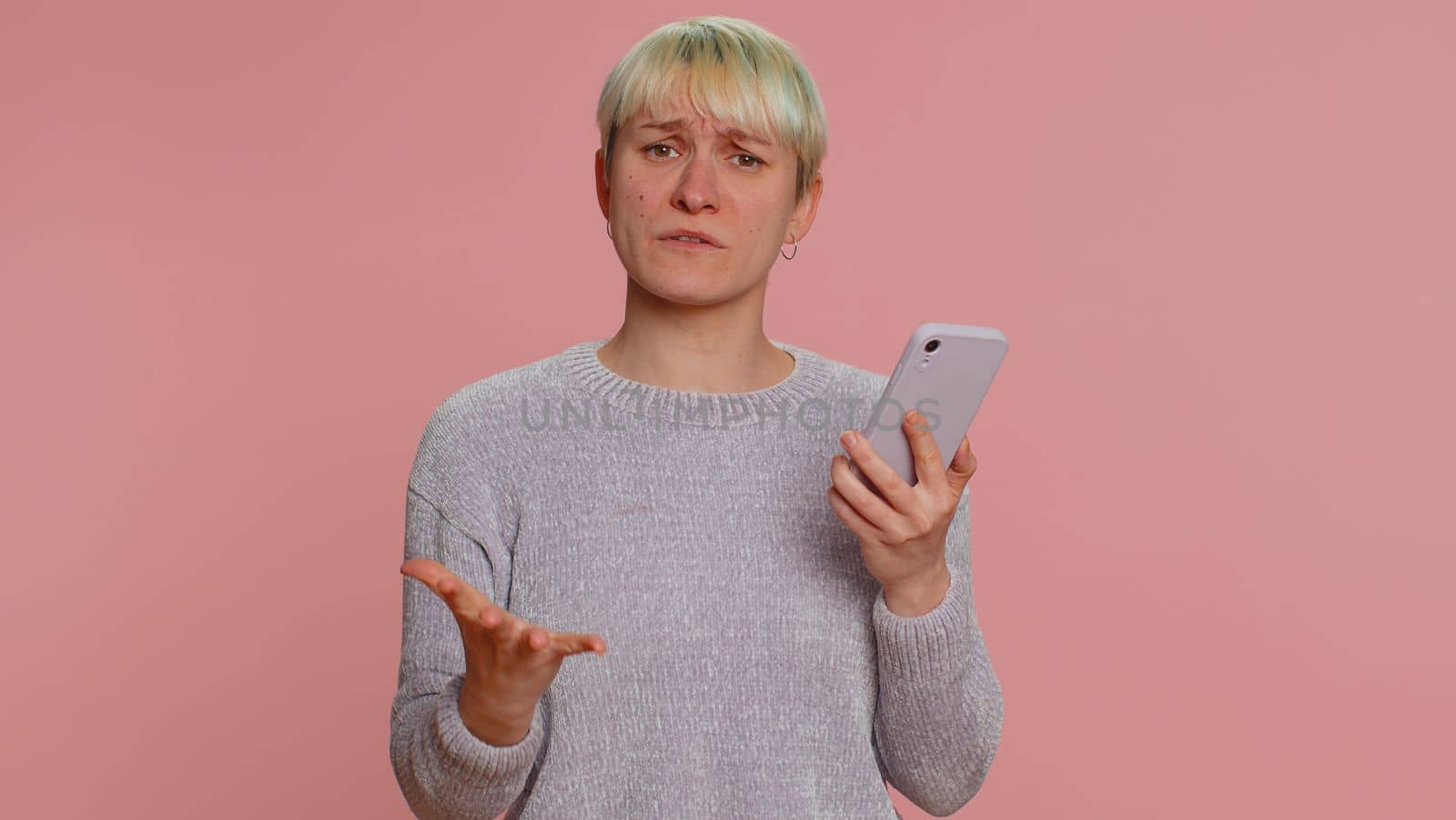 Hipster woman with short hair use mobile cell phone typing browsing, loses becoming surprised sudden lottery results, bad fortune, loss, fail. Young girl isolated alone on pink studio wall background