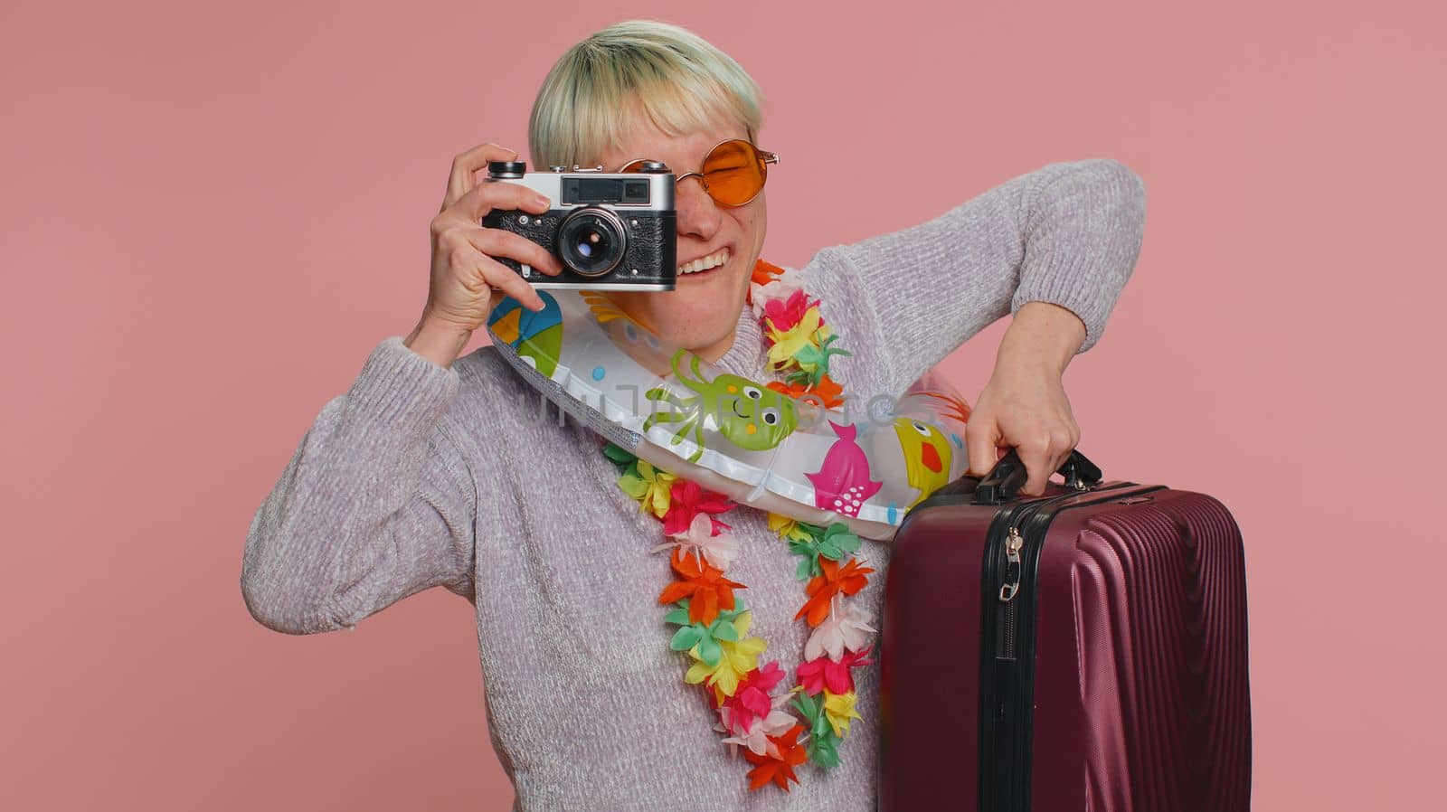 Millennial woman tourist photographer with short hair taking photos on retro camera and smiling. Travel, summer holiday vacation. Young girl isolated on pink studio background. Lgbt gay lesbian people