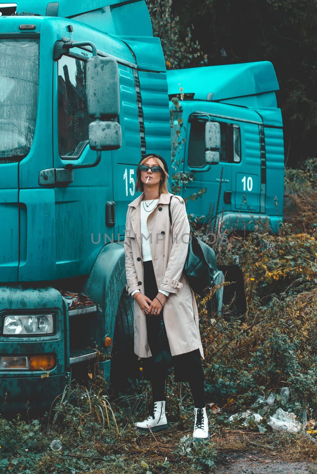 stylish blonde woman wearing long beige coat, white boots and black hat posing near the blue truck. Trendy casual outfit. Selective focus, grain by Ashtray25