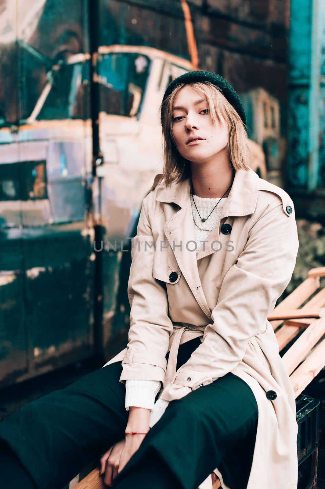 Beautiful young stylish blonde woman wearing long beige coat, white boots, black hat posing through the city streets. Trendy casual outfit. Selective focus, grain by Ashtray25