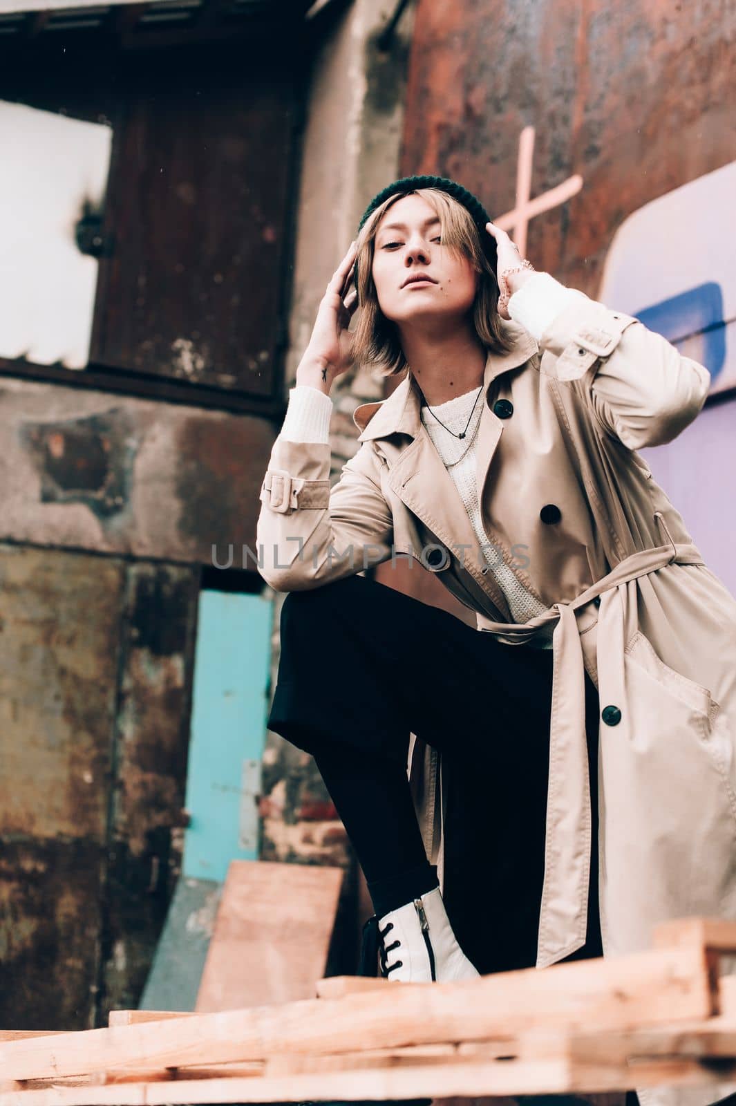 Beautiful young stylish blonde woman wearing long beige coat, white boots, black hat posing through the city streets. Trendy casual outfit. Selective focus, grain by Ashtray25