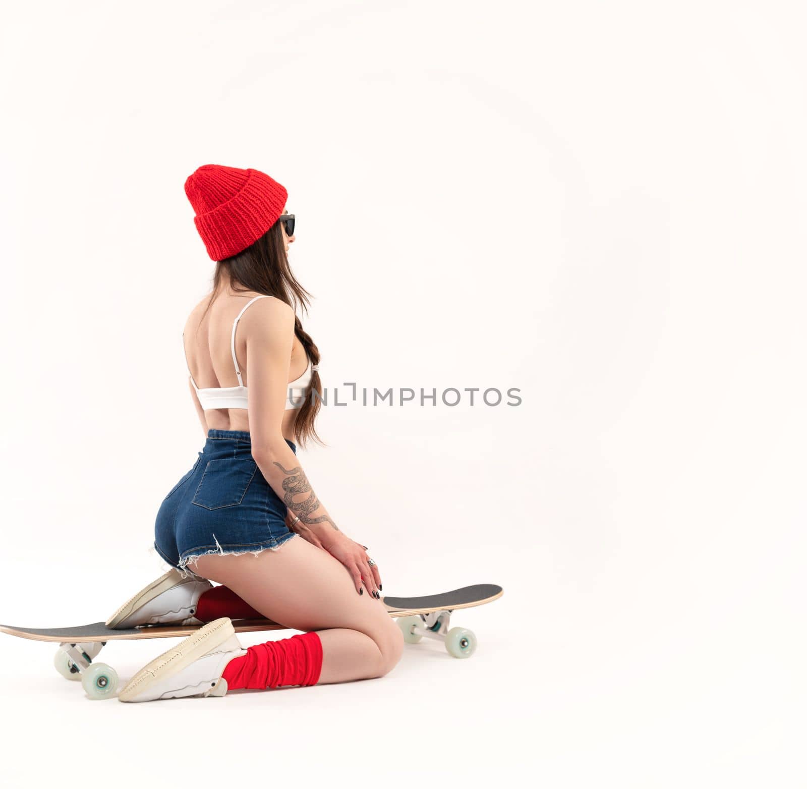 sexy girl in a fashionable red hat sitting on a longboard on a white background copy paste