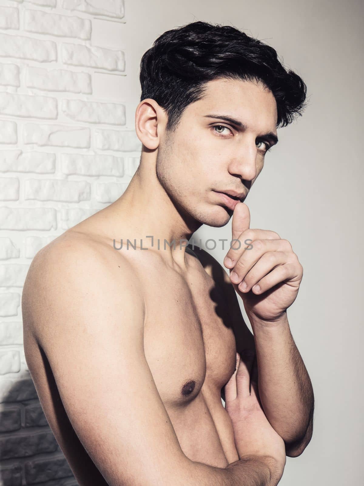 Handsome young man's headshot against white wall with a hand on his chin, looking at camera to a side