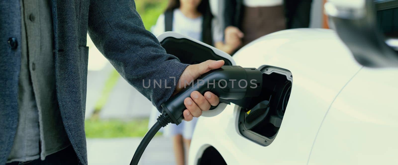 Focus hand charging progressive EV car with blurred family background. by biancoblue