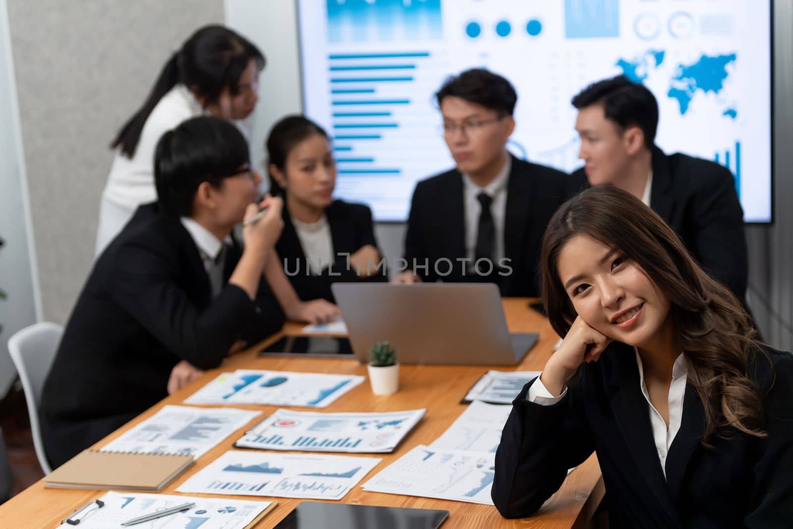 Focus portrait of female manger, businesswoman in the harmony meeting room with blurred of colleagues working together, analyzing financial paper report and dashboard data on screen in background.