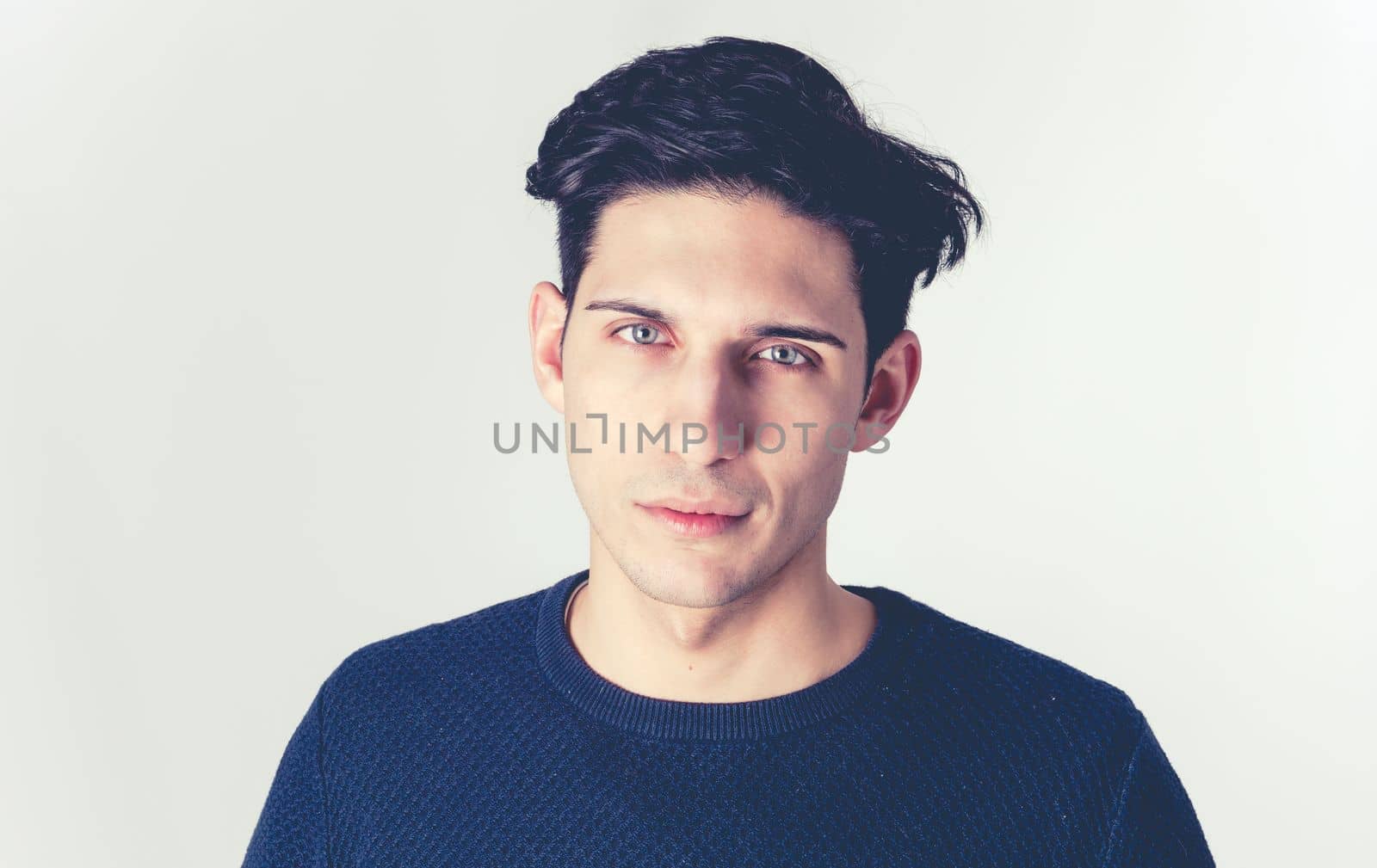 Handsome and fit young man standing on grey background, looking at camera with piercing green eyes, wearing blue t-shirt