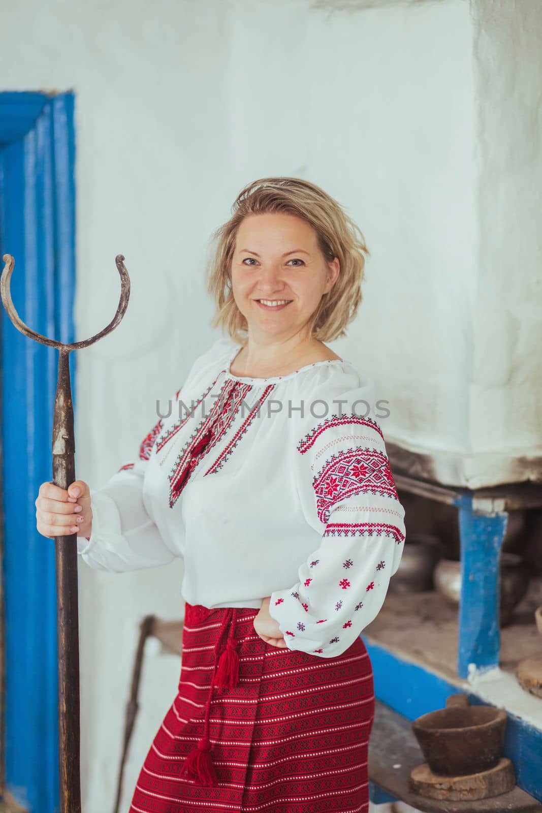 Hostess in embroidered clothes with poker near the stove. Retro photo of ancient Ukrainian life