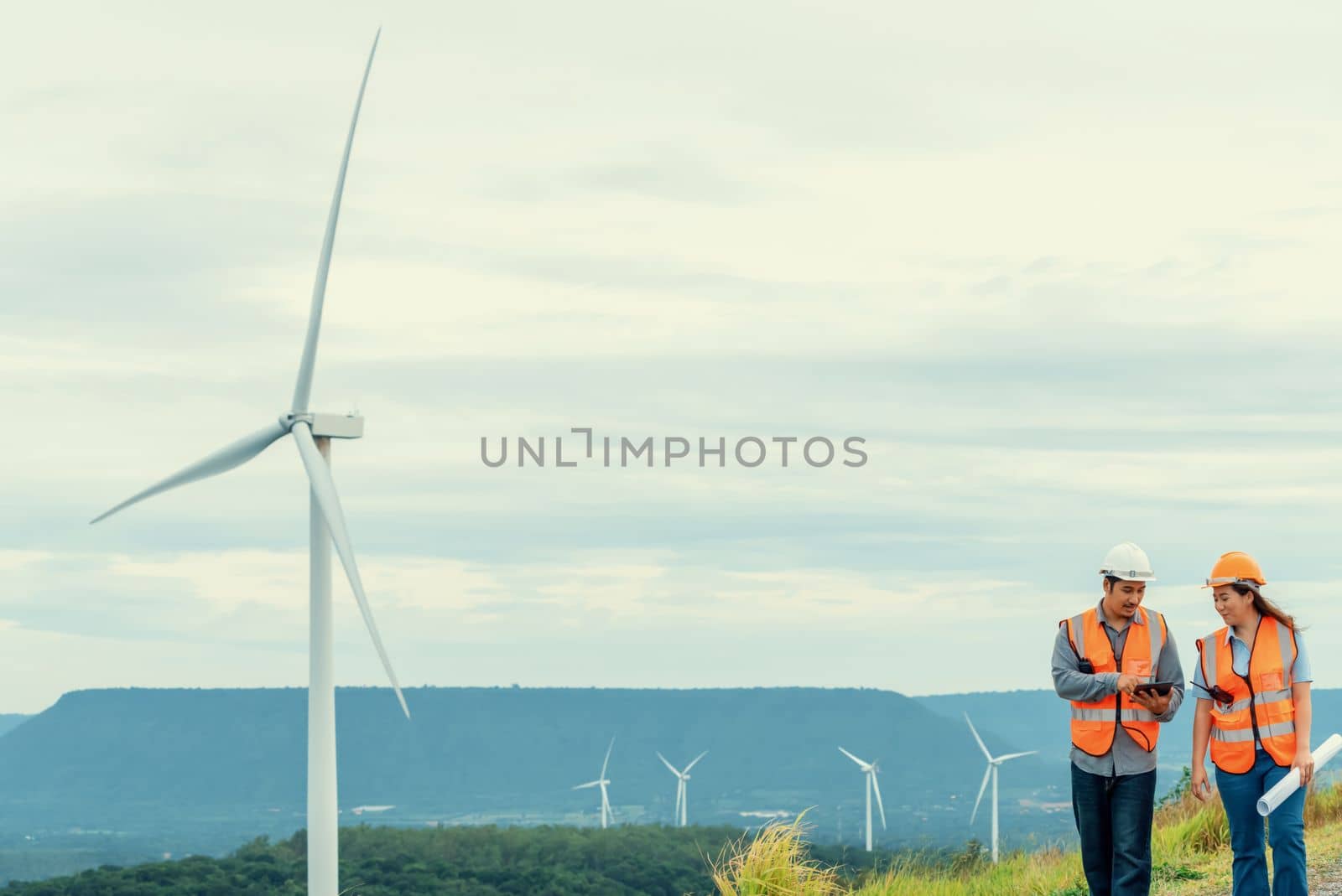 Male and female engineers working on a wind farm atop a hill or mountain in the rural. Progressive ideal for the future production of renewable, sustainable energy.