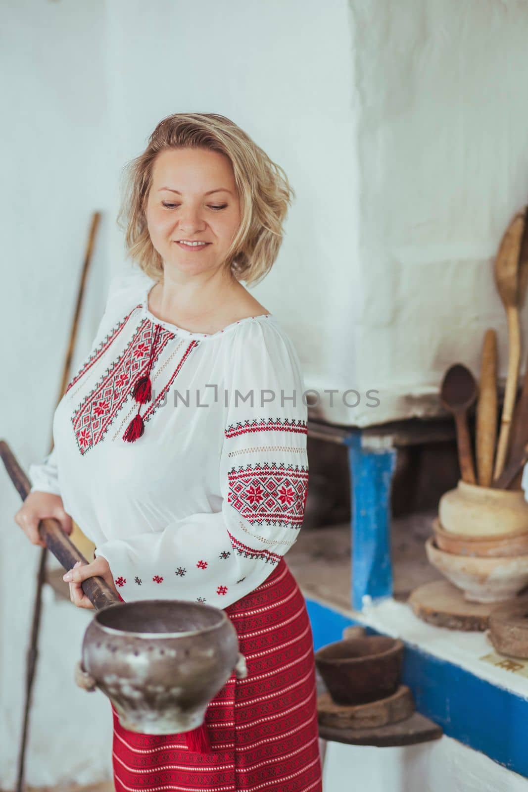 Hostess in embroidered clothes pulled a pot of food out of the oven. Ancient Ukrainian life