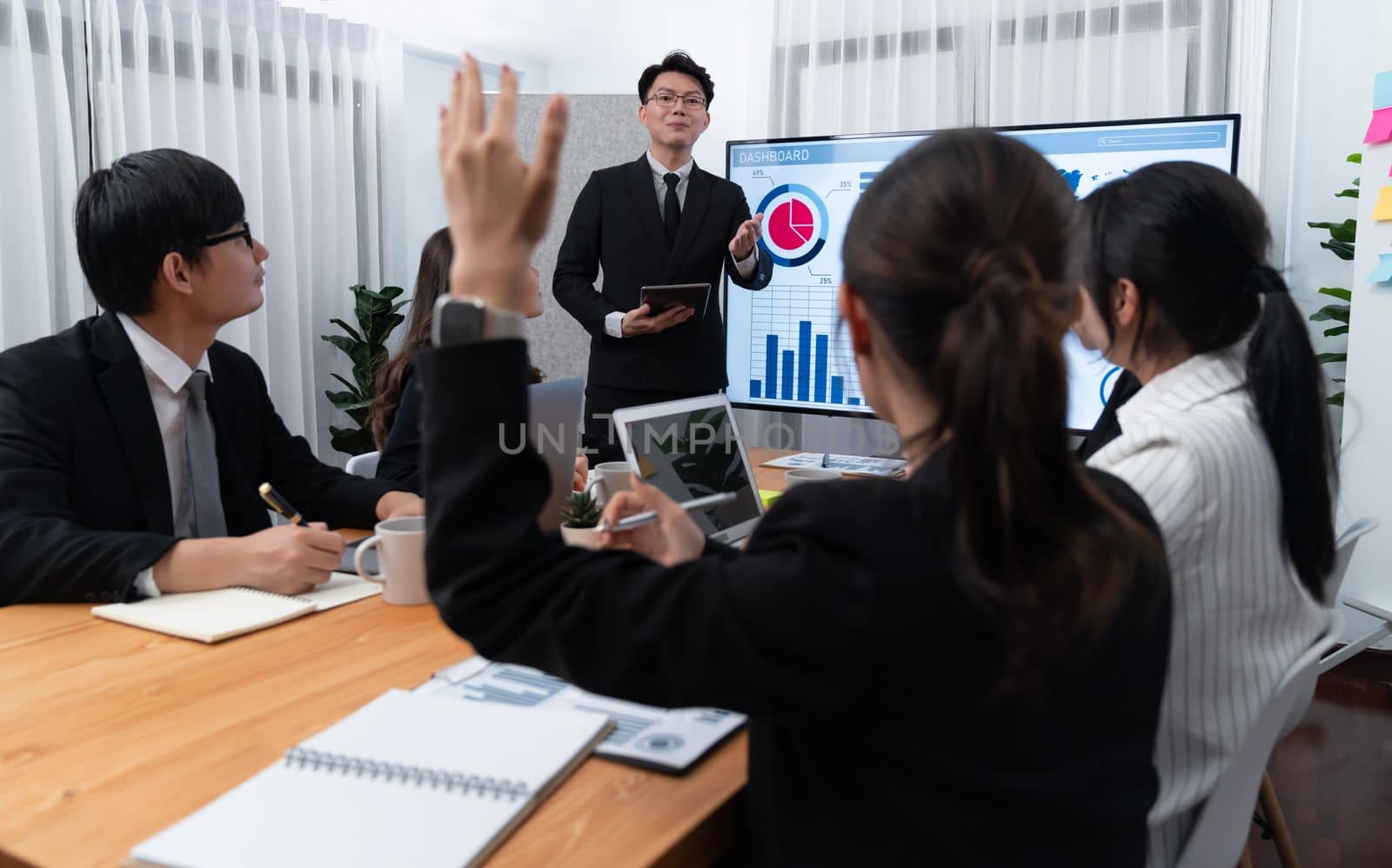 Harmony group businesspeople in meeting room during presentation with dashboard BI financial data displayed on screen, motivated employee raising hand asking question as productive teamwork concept.