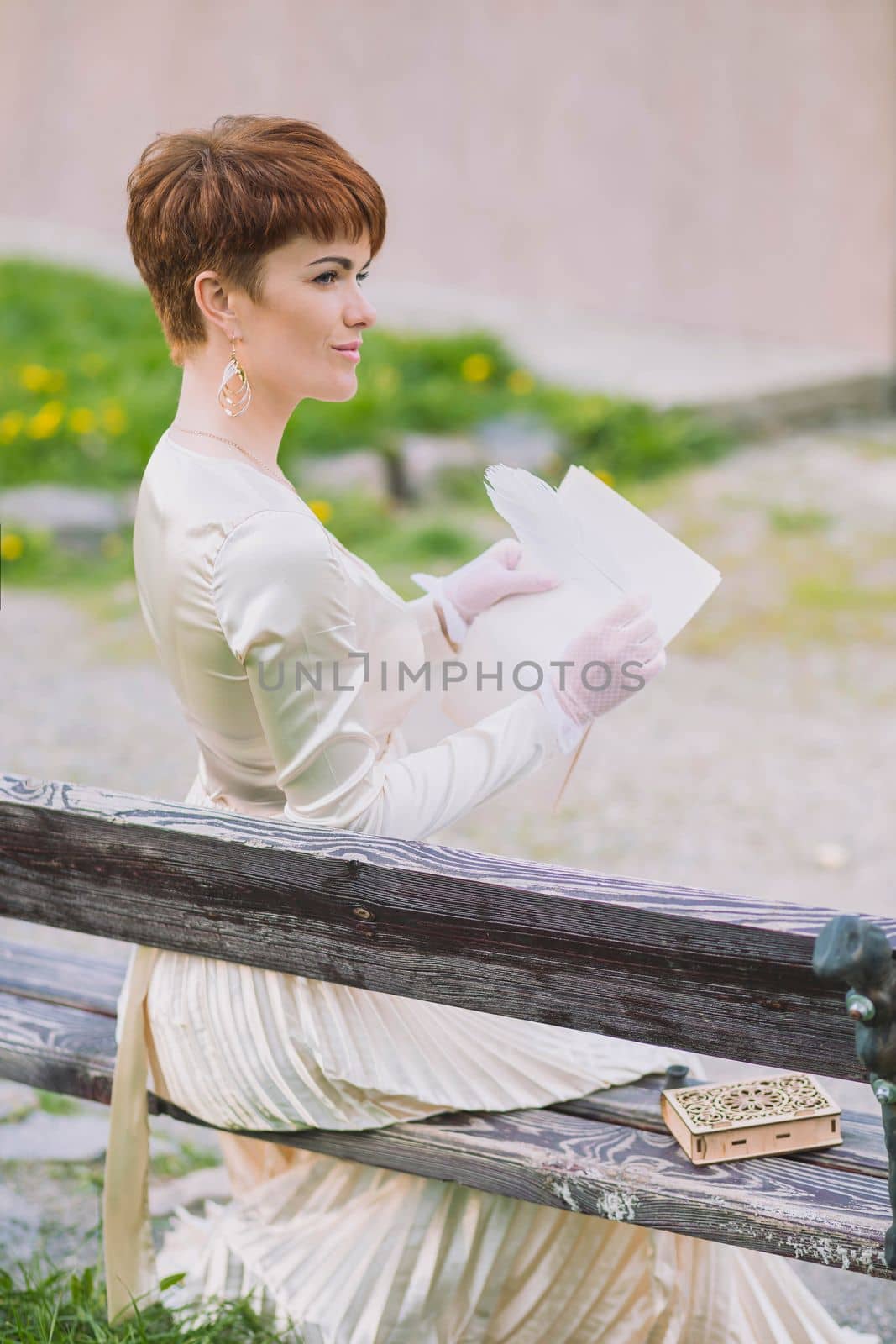 Retro photo of beautiful woman in golden dress writing letter with quill pen in the garden