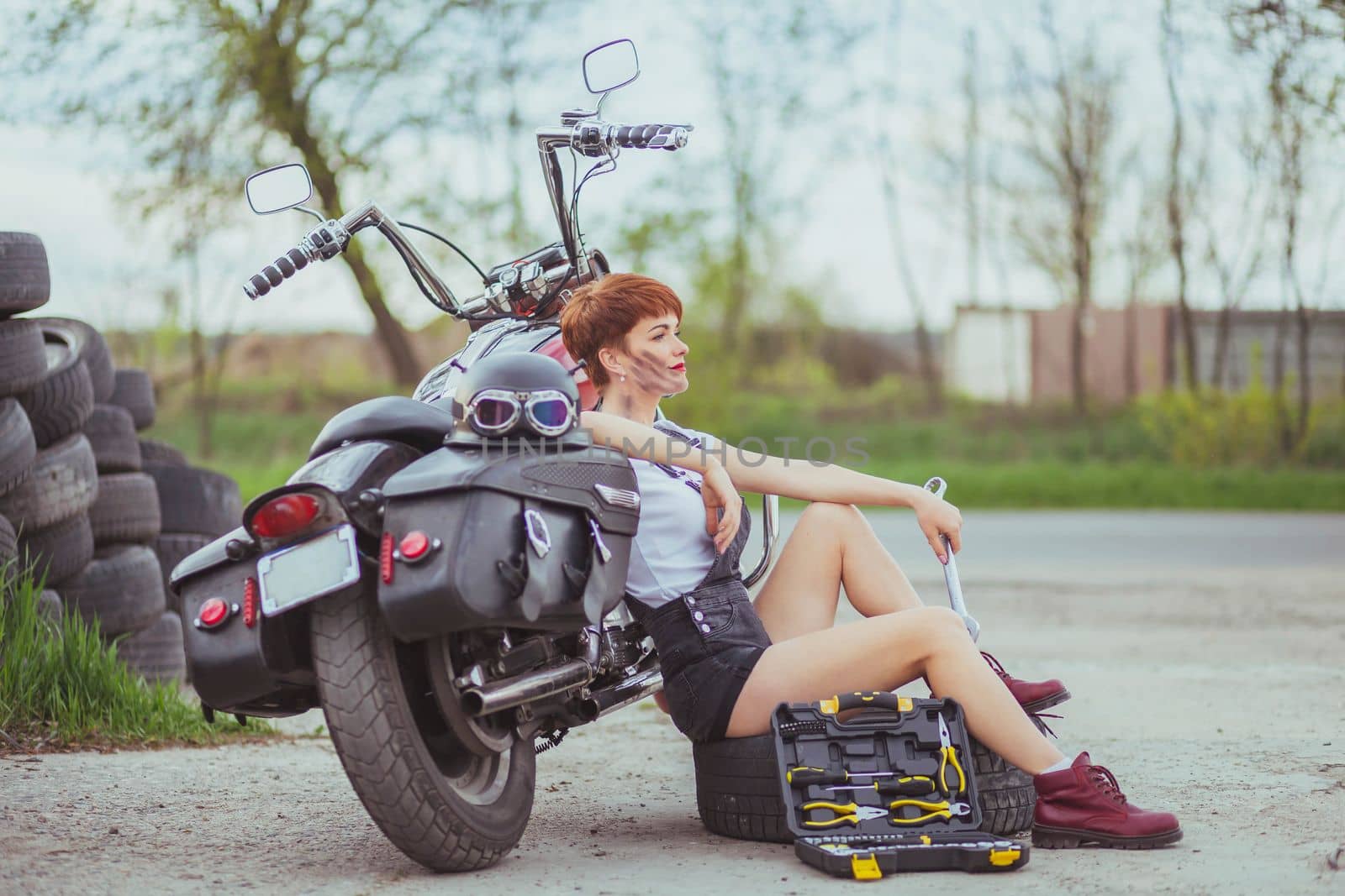 Beautiful slim woman mechanic sitting near a motorcycle.