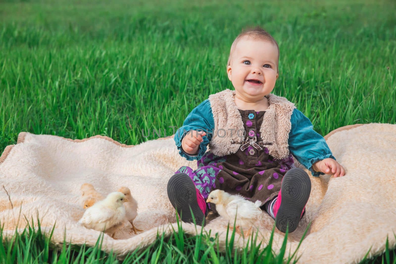 baby in a colorful dress on the lawn with chickens.