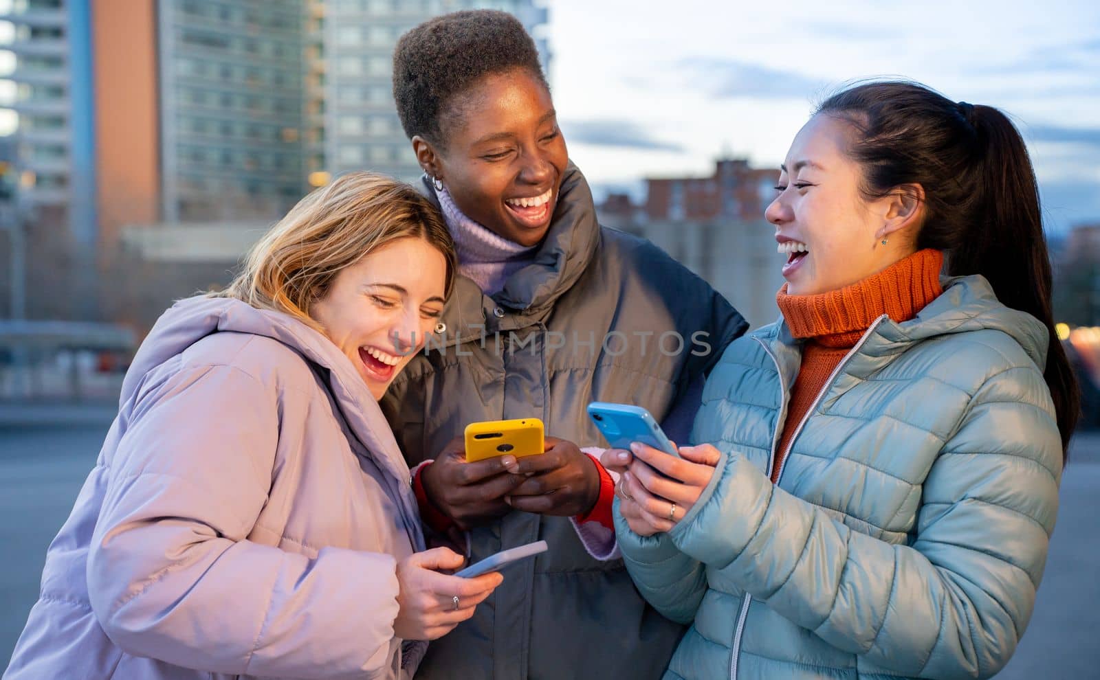 Cheerful female friends using cell phones and laughing in the city. Technology addicted concept by PaulCarr