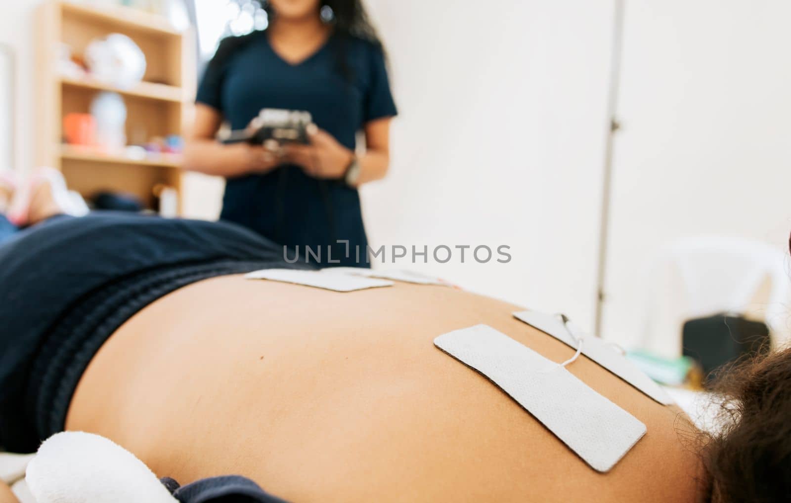Electrode treatment to patient lying down, Professional physiotherapist electrostimulating a lying patient. Physiotherapist electrostimulating a patient, Lower back therapy with electrode pads