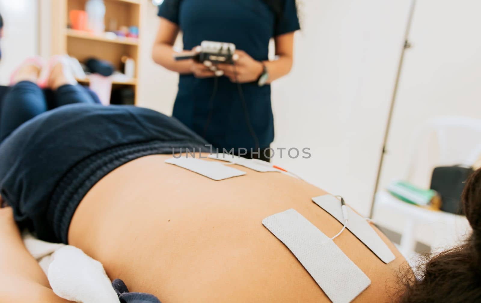 Physiotherapist electrostimulating a patient, Electrode treatment to patient lying down, Professional physiotherapist electrostimulating a lying patient. Lower back therapy with electrode pads