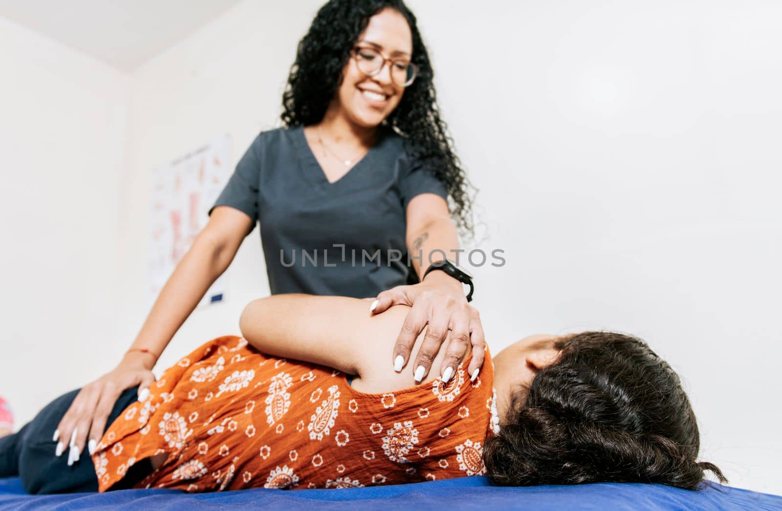 Physiotherapist rehabilitating shoulder to patient lying on her side. Shoulder and back treatment and rehabilitation concept, Woman doing shoulder rehabilitation physiotherapy by isaiphoto