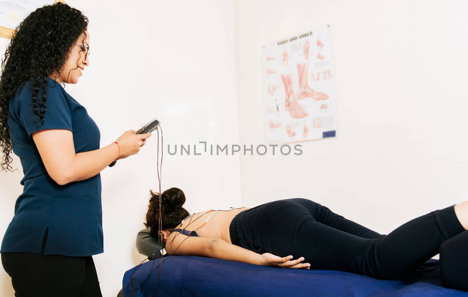 Professional physiotherapist electrostimulating a lying patient. Physiotherapist electrostimulating a patient. Lower back therapy with electrode pads. Electrode treatment to patient lying down