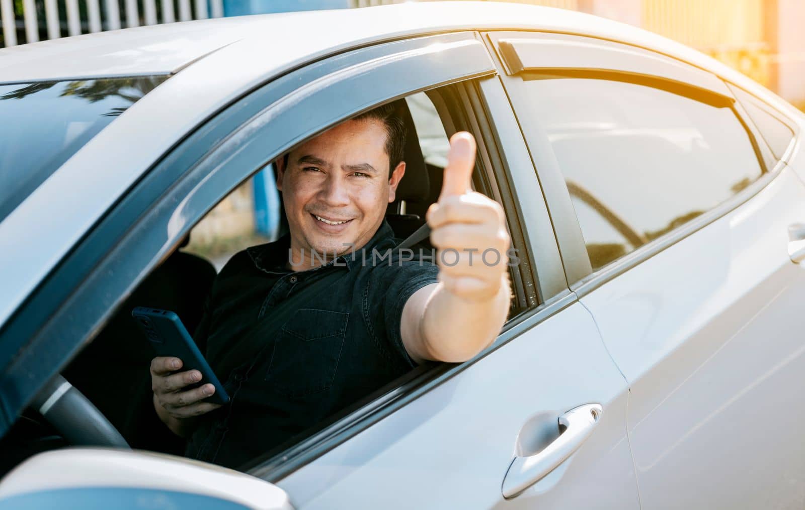 Smiling driver holding cellphone showing thumb up. Driver man showing thumb up while holding cellphone. Happy driver giving a thumbs up on the road. safe driving concept