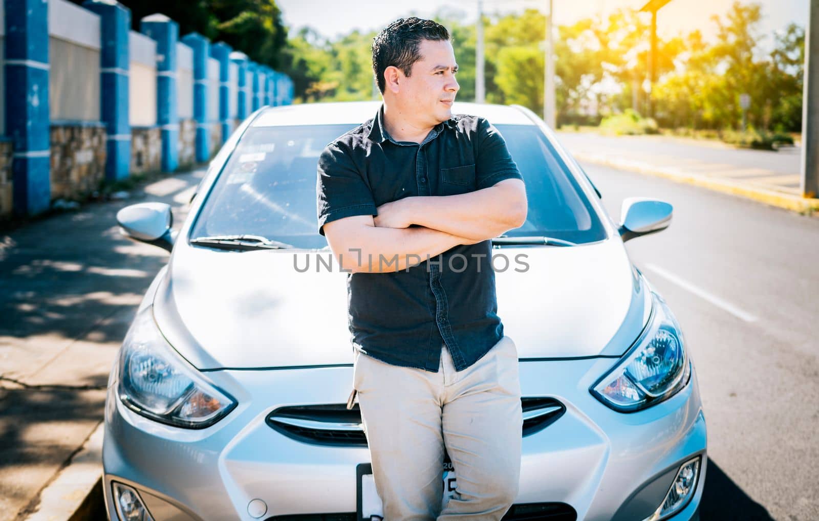 Portrait of smiling man leaning on the car. Young man with crossed arms leaning on his car. Handsome young man with arms crossed leaning on his car.