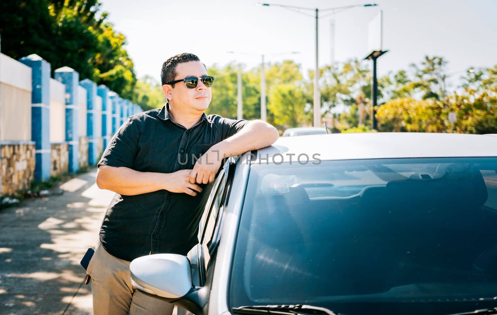 Smiling driver leaning on the car door. Smiling owner with new car. Young latin man leaning on car door in the street, Happy driver leaning on the car door in the street