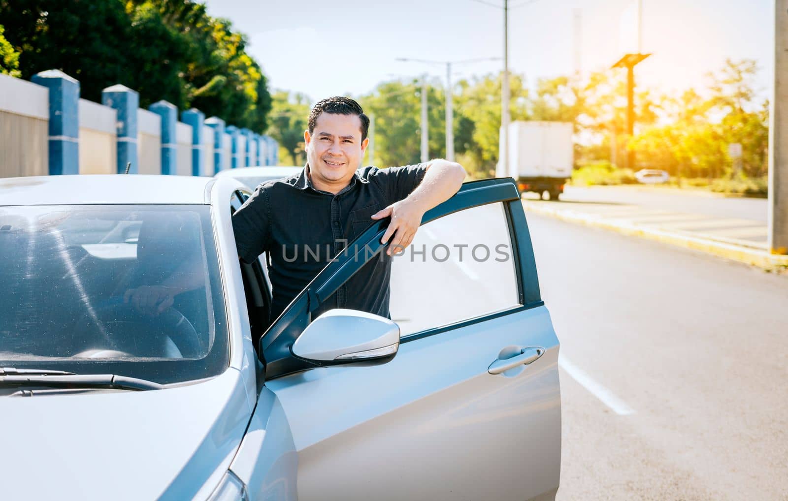 Smiling driver leaning on the car door. happy driver leaning on the car door in the street, Smiling owner with new car. Young latin man leaning on car door in the street