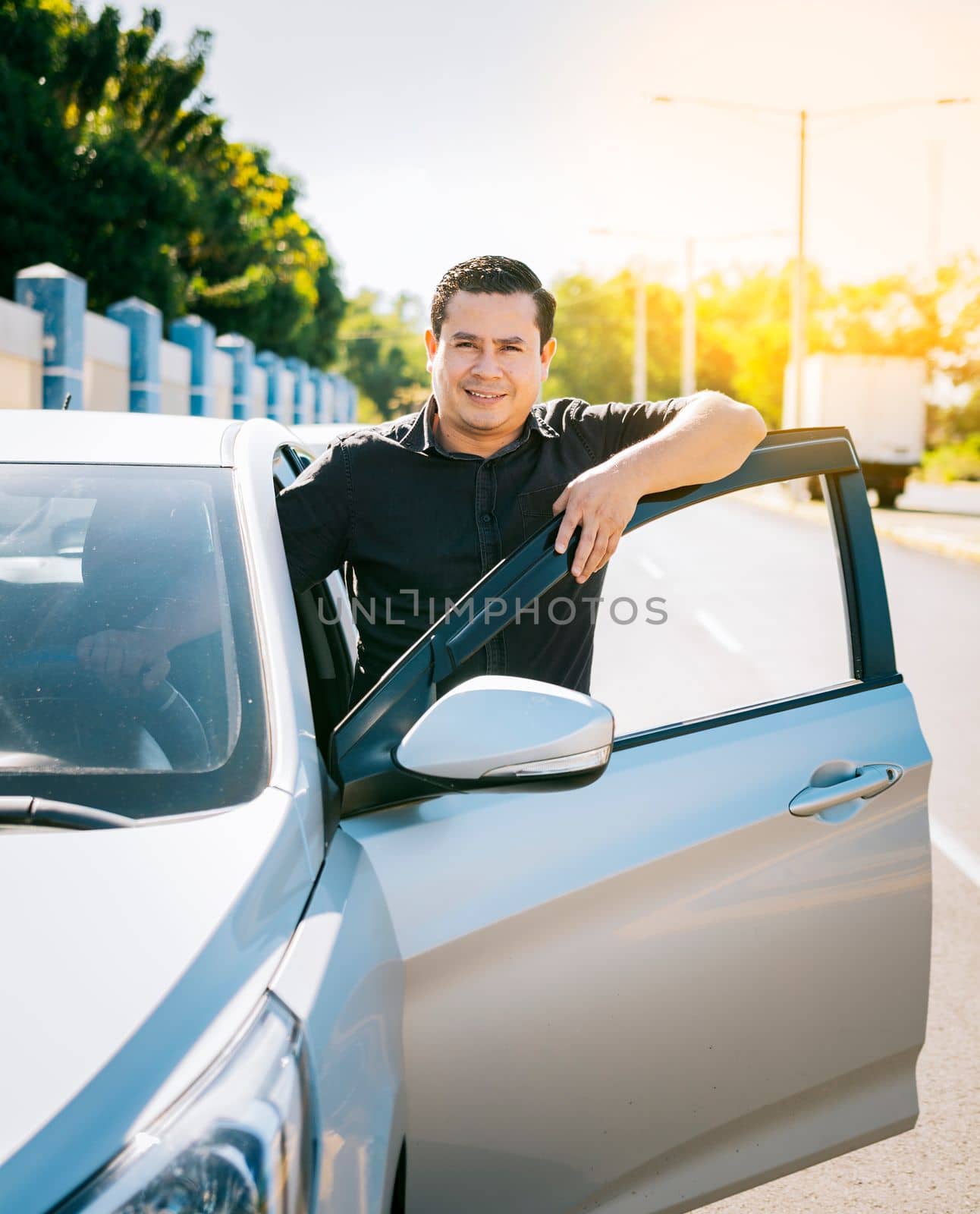 Happy driver leaning on the car door in the street, Smiling driver leaning on the car door. Smiling owner with new car. Young latin man leaning on car door in the street