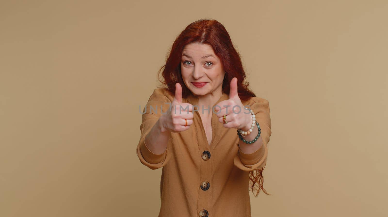 Like. Hipster pretty redhead woman in blouse raises thumbs up agrees with something or gives positive reply recommends advertisement likes good. Young girl isolated alone on beige studio background