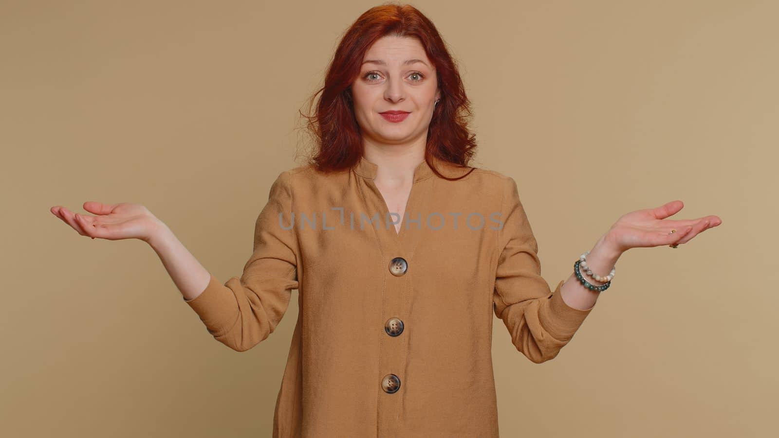 I dont know what to say. Confused woman feeling embarrassed about ambiguous question, having doubts, no idea, being clueless and uncertain. Young redhead girl isolated on beige studio wall background