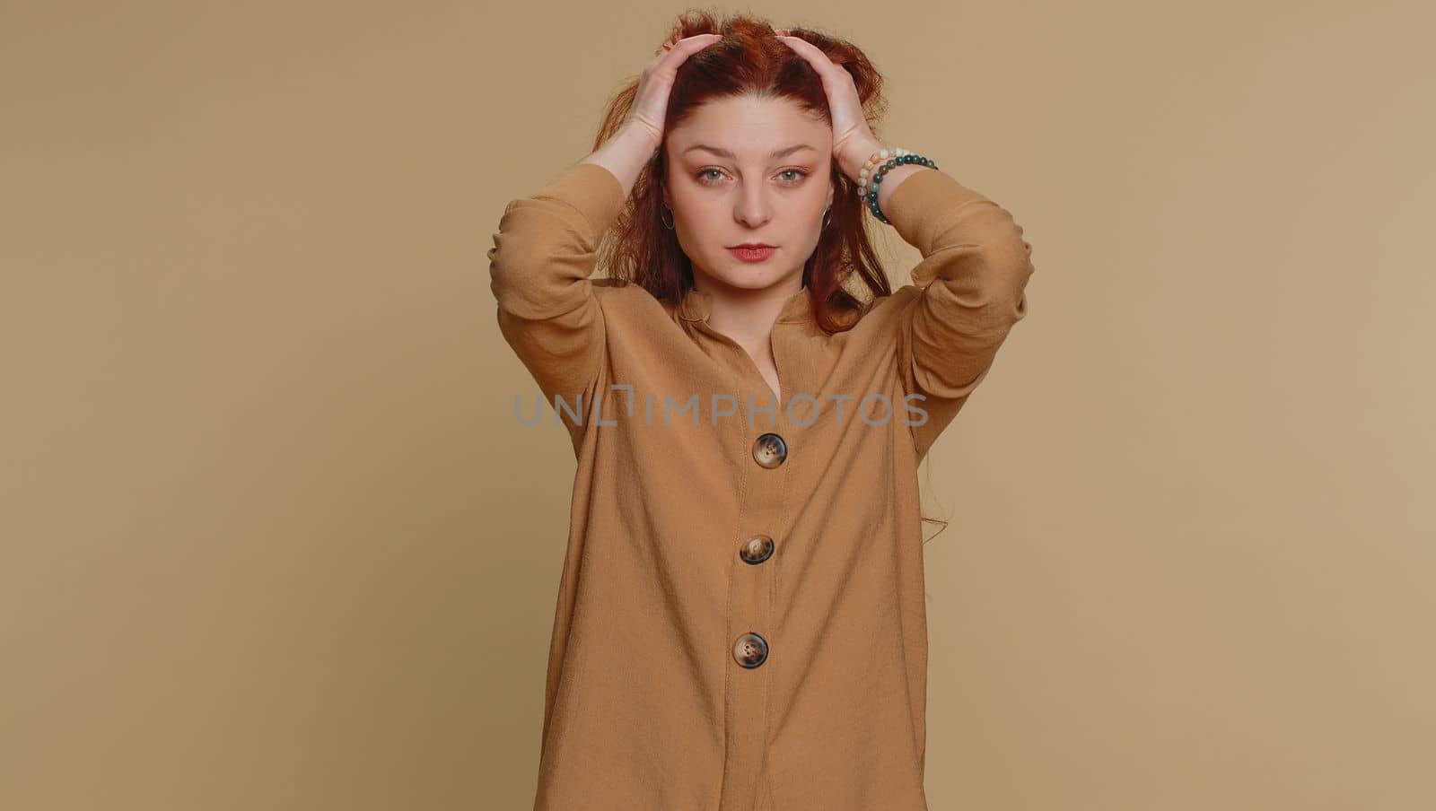 Hipster young redhead woman in blouse rubbing temples to cure headache problem, suffering from tension, migaine, stress, grimacing in pain, high blood pressure isolated alone on beige wall background