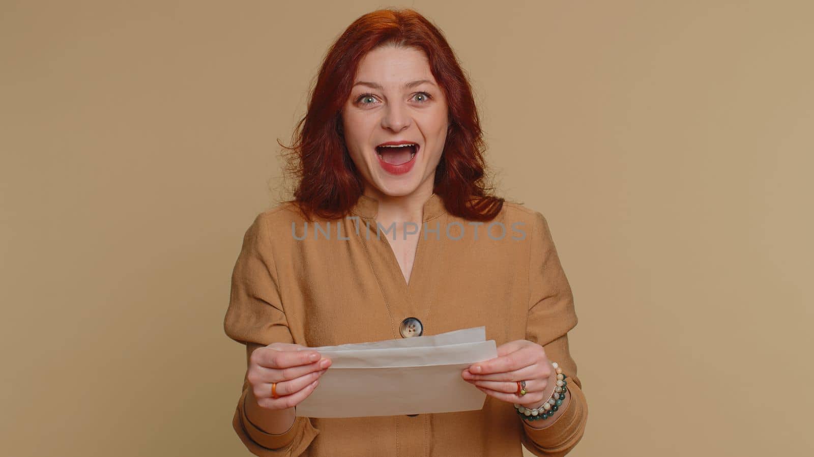 Young redhead student woman open envelope take out letter reads it feel happy. Girl career growth advance promotion, bank loan approve, monetary award, long-awaited invitation great news, lottery win