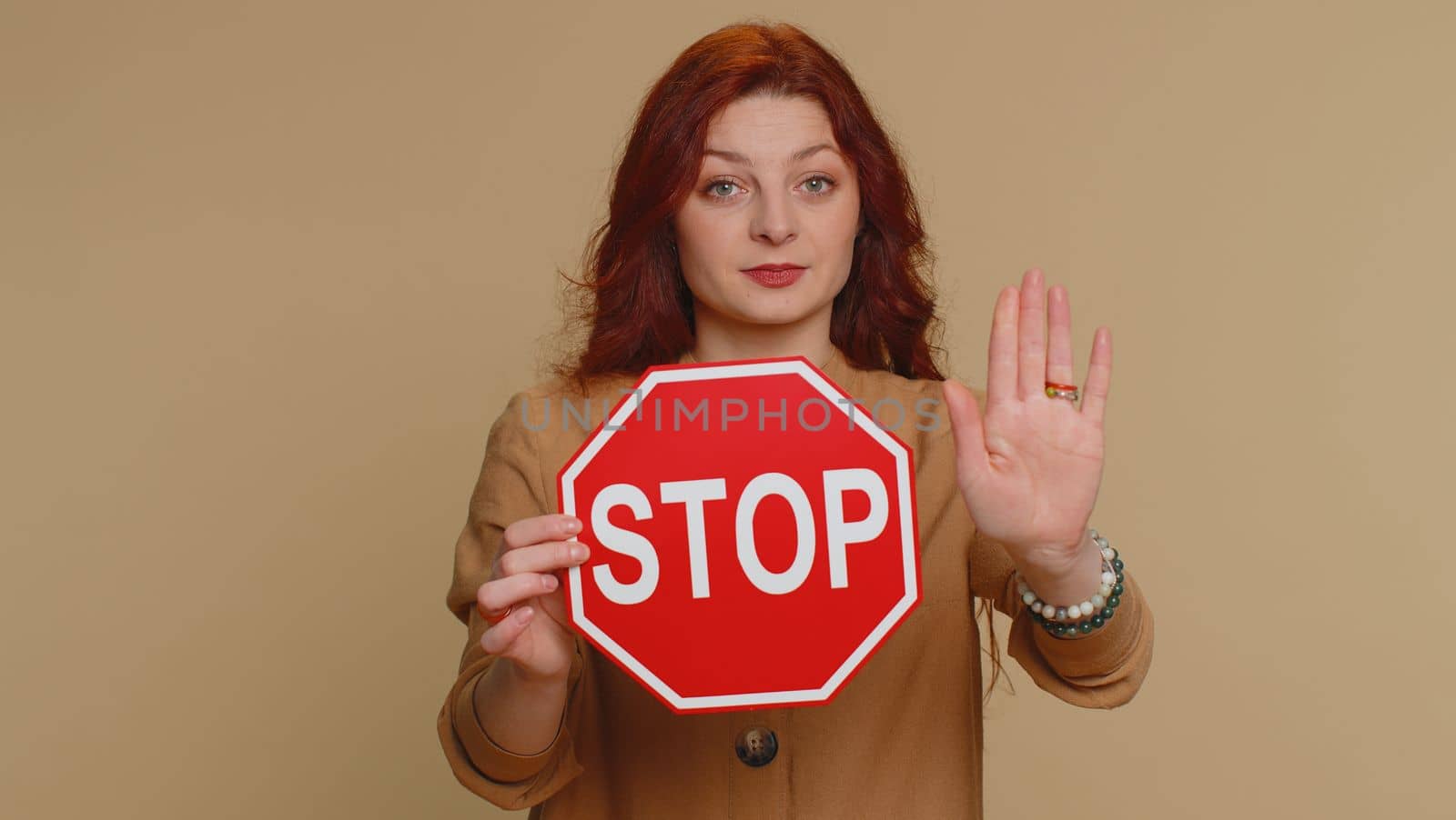 Serious redhead woman say No, hold inscription text red No stop danger sign, warning of finish, prohibited access declining communication, body language, trouble, protest. Girl on beige background