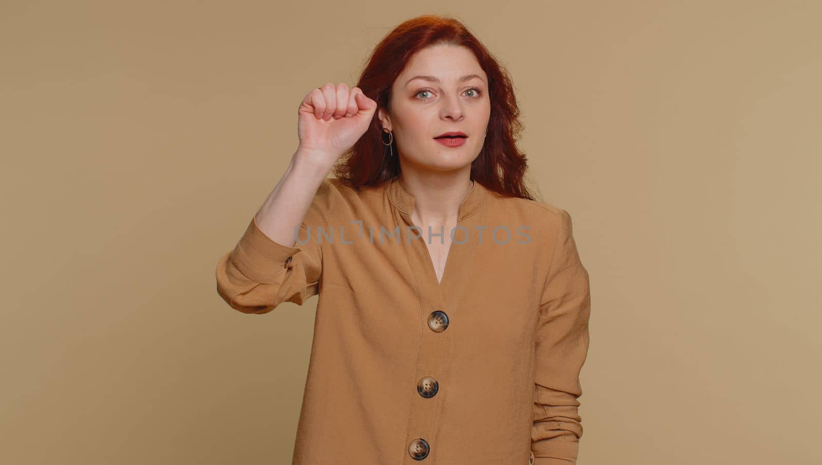 Knock-knock who is there. Confused redhead woman knocking door gesture asking who is at home, feeling embarrassed, no idea, being clueless and uncertain. Young ginger girl on beige studio background
