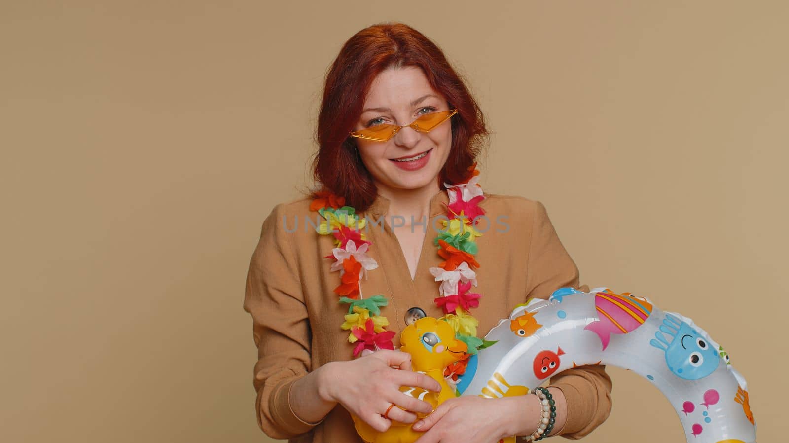 Traveler tourist young woman celebrating, dancing fooling with swimming inflatable duck toy. Concept summer vacation, journey, trip to seaside. Redhead girl in sunglasses on beige studio background