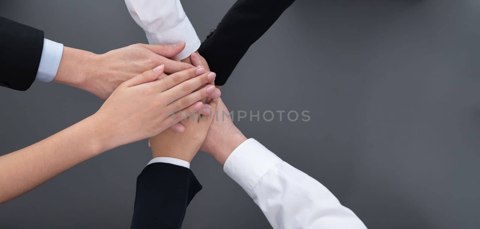 Top view partial hands wearing formal suit joining stack and form circle as symbol of team building, unity and harmony in office workplace. Successful business team of synergy holding hand together.
